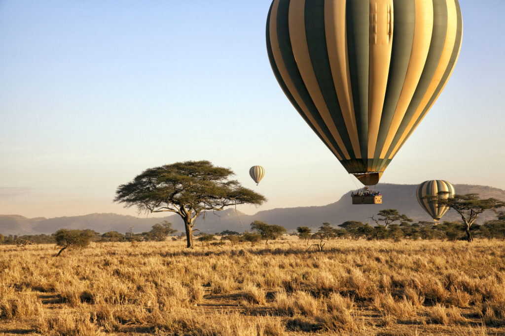Drei Heißluftballons treiben im Morgengrauen über die Ebenen des Serengeti-Nationalparks.