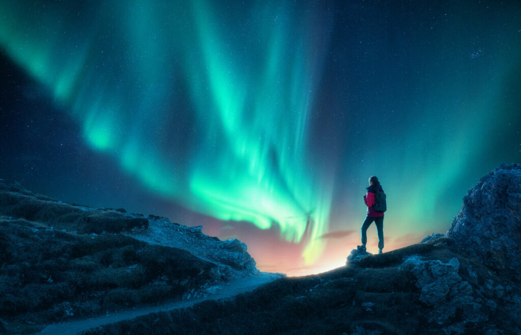 Frau auf Felsen mit Blick auf Polarlichter