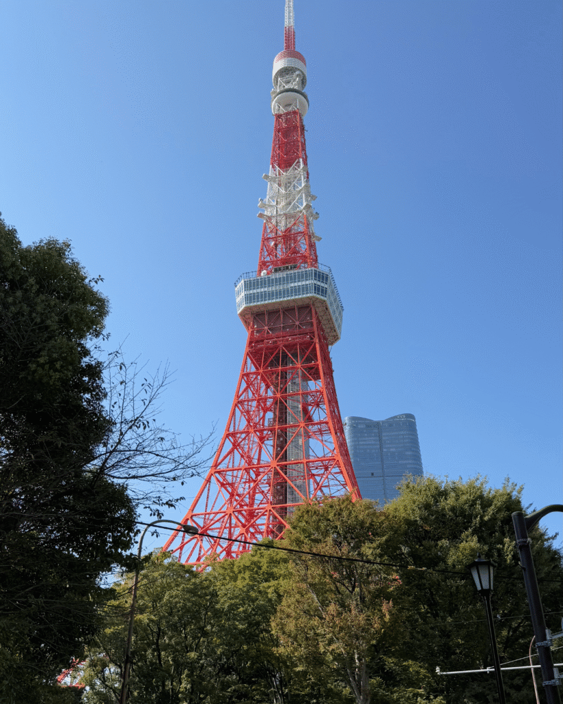 Tokio Tower bei klarem Himmel, ikonischer rot-weißer Fernsehturm umgeben von grünen Bäumen und modernen Gebäuden.