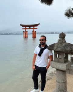 Torii im Wasser vor der Insel Itsukushima, ikonisches Wahrzeichen Japans mit Bergen und Stadt im Hintergrund.