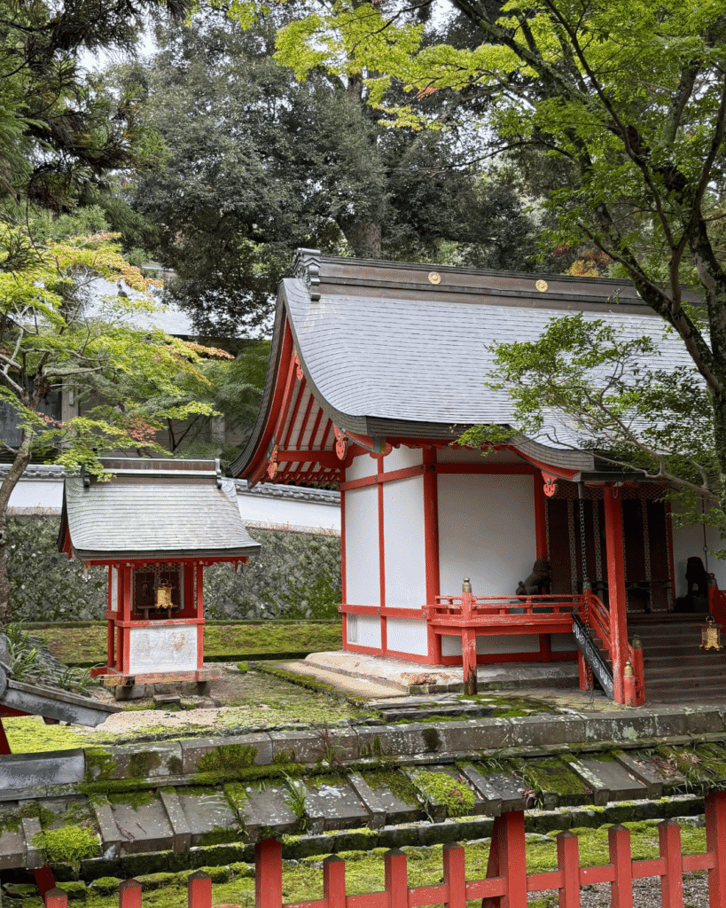 Shinto-Schrein in Kyoto mit roten Holzdetails, Moos und grüner Vegetation, umgeben von Steinmauern.