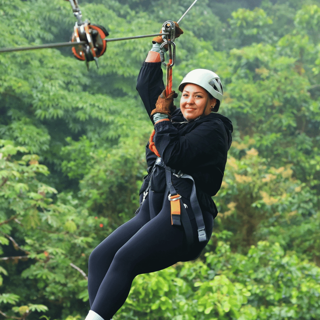 Frau hängt an einer Zipline mit Sicherheitsausrüstung und Helm, umgeben von dichtem grünen Regenwald.