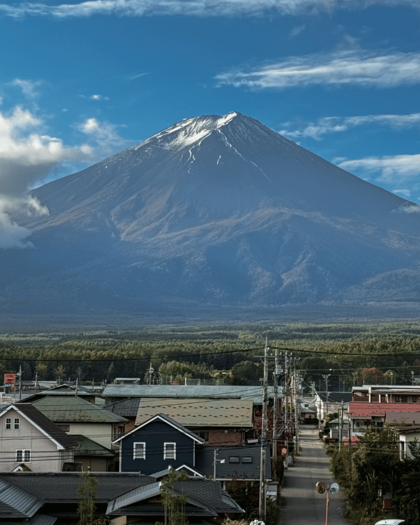 Majestätischer Mount Fuji mit schneebedecktem Gipfel über japanischer Stadtlandschaft unter blauem Himmel.