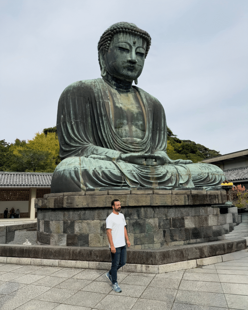 Große Buddha-Statue in Kamakura aus Bronze auf steinernem Sockel, traditioneller Tempelhof im Hintergrund.