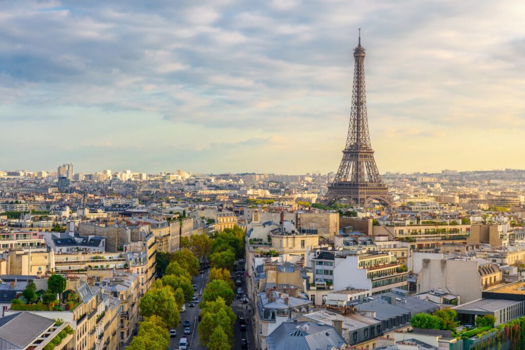 Blick über Paris mit dem Eiffelturm im Zentrum, umgeben von historischen Gebäuden und grünen Alleen unter leicht bewölktem Himmel.