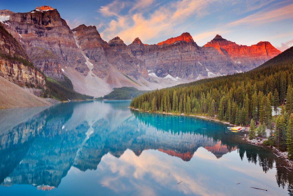 Moraine Lake im Banff-Nationalpark, Kanada, mit türkisfarbenem Wasser, umgeben von Nadelwäldern und Bergen, im warmen Licht des Sonnenaufgangs.