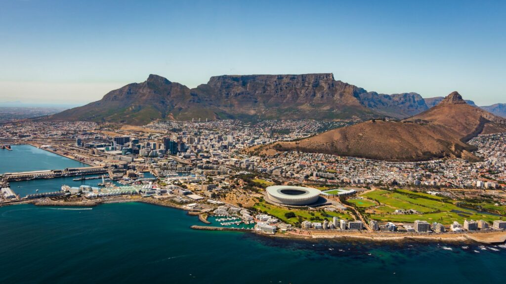 Luftaufnahme von Kapstadt mit Tafelberg, Lion’s Head, dem Stadion und der Küste am tiefblauen Atlantik unter klarem Himmel.