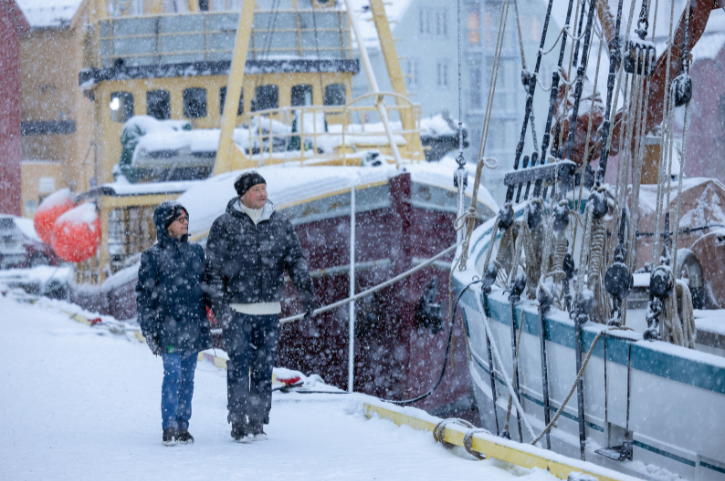 Winterliche Hafenpromenade in Tromsø, Norwegen, mit verschneiten Booten und traditionellen Schiffen im Schneefall