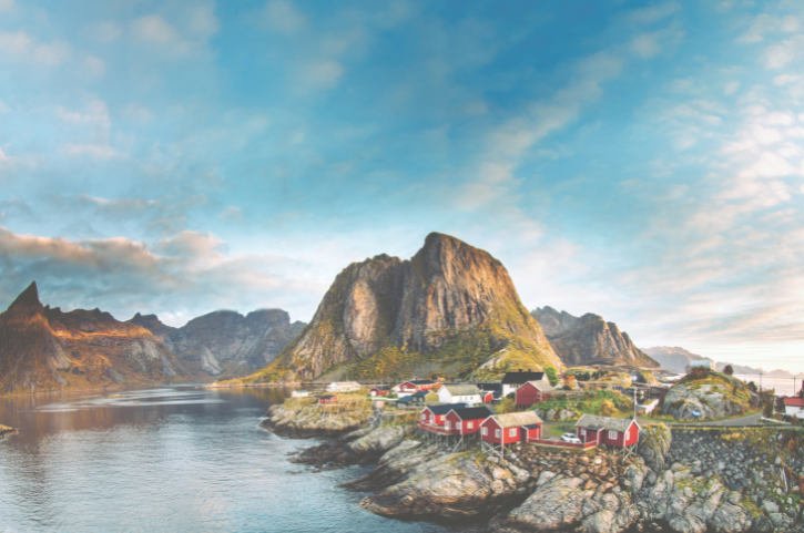 Panorama von Reine auf den Lofoten in Norwegen mit roten Fischerhütten am Wasser und imposanten Bergen bei klarem Himmel