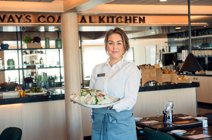 Servicemitarbeiterin im Torget Restaurant an Bord des Hurtigruten Schiffs MS Polarlys serviert frisches norwegisches Gericht in moderner Küstenküche