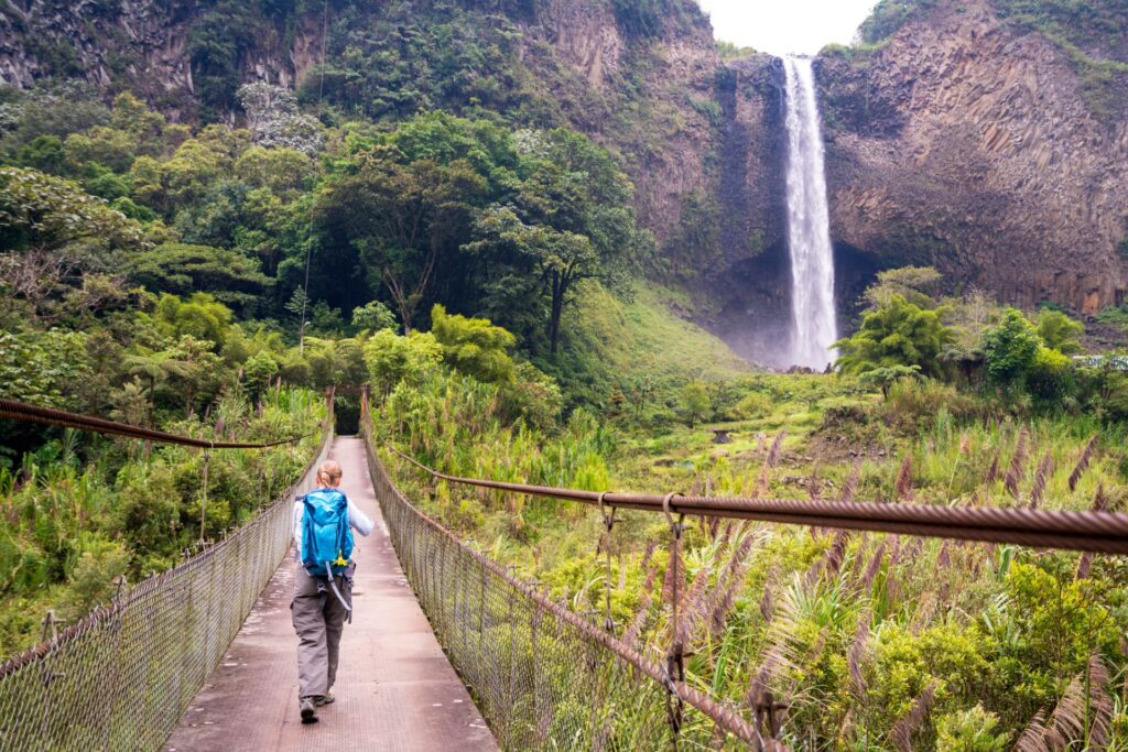 Eine ältere Frau wandert auf einer Hängebrücke auf dem Weg zum Wasserfall „Brautschleier“ (Manto de la novia) im Kaskadenweg bei Baños, Ecuador.