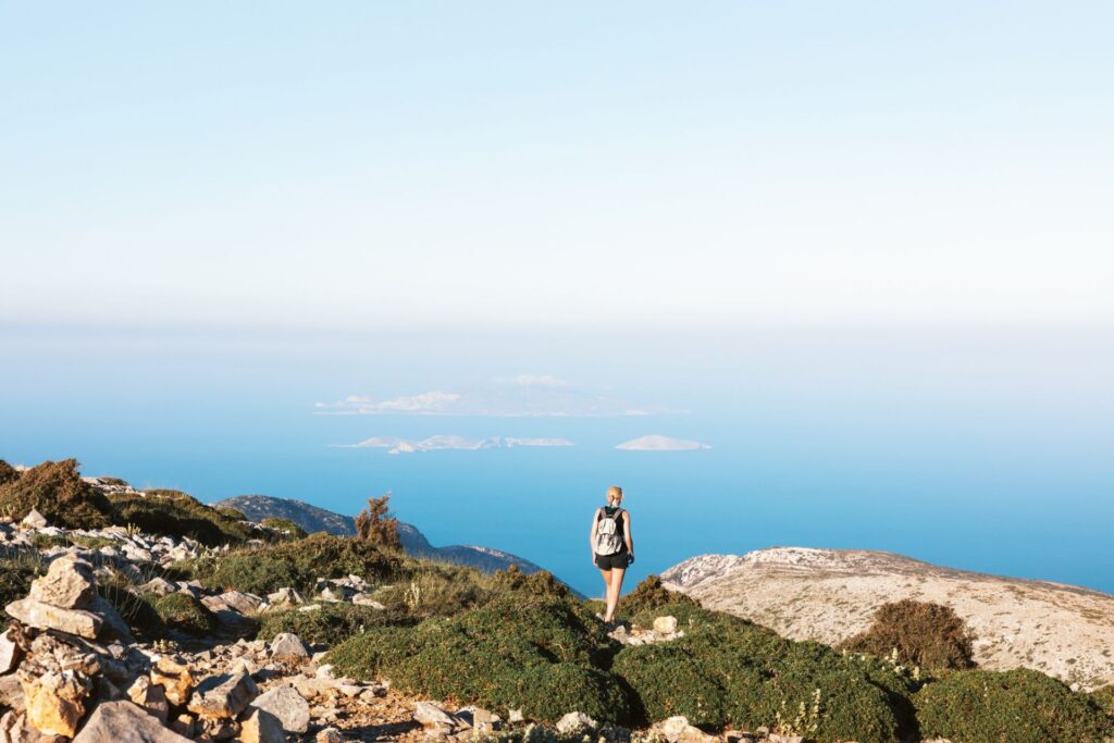Frau beim Wandern auf dem Berg Zas, dem höchsten Punkt der Kykladen (Insel Naxos, Griechenland) mit Blick auf blaues Meer und vereinzelten Inseln.