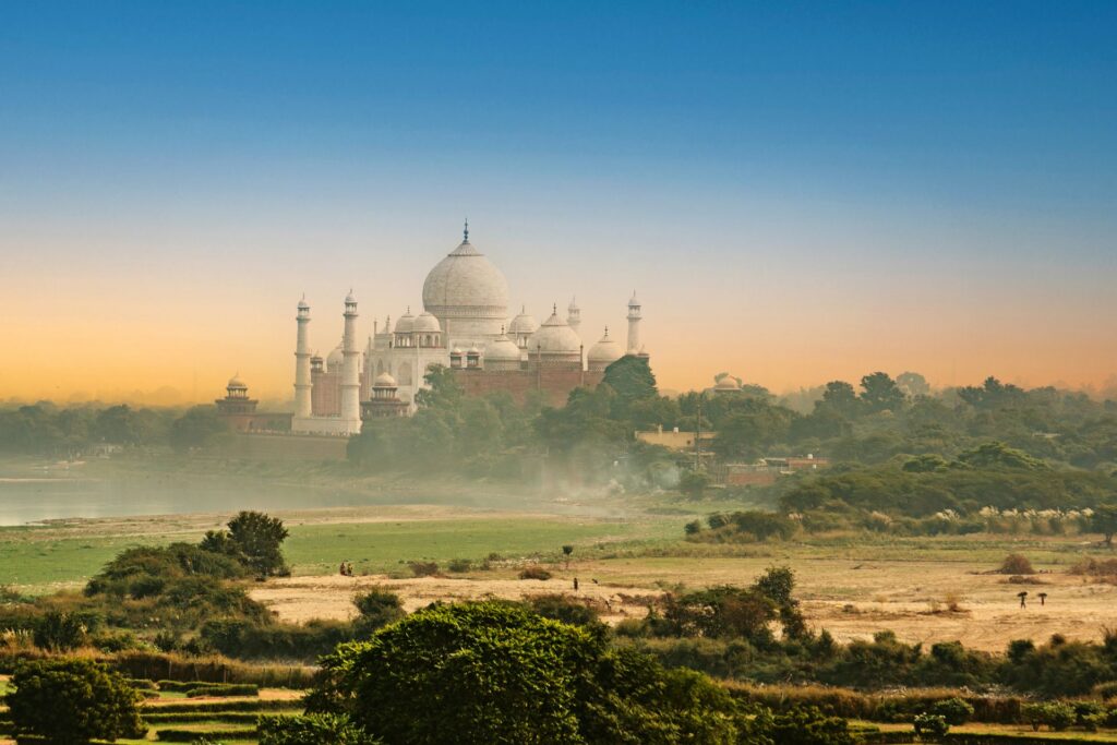 Das Taj Mahal mit seinen ikonischen Kuppeln dominiert eine üppige Landschaft bei einem lebendigen Sonnenuntergang.
