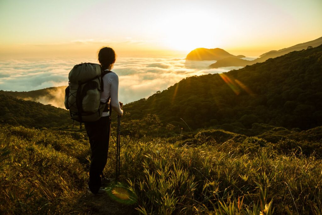 Wanderin mit Rucksack und Wanderstock genießt den Sonnenuntergang über dem nebeligen Regenwald im Amazonas in Brasilien.