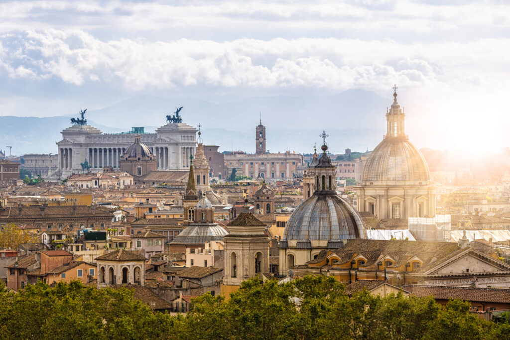 Panoramablick auf Rom mit Petersdom, Vittoriano und vielen Kuppeln im warmen Abendlicht.