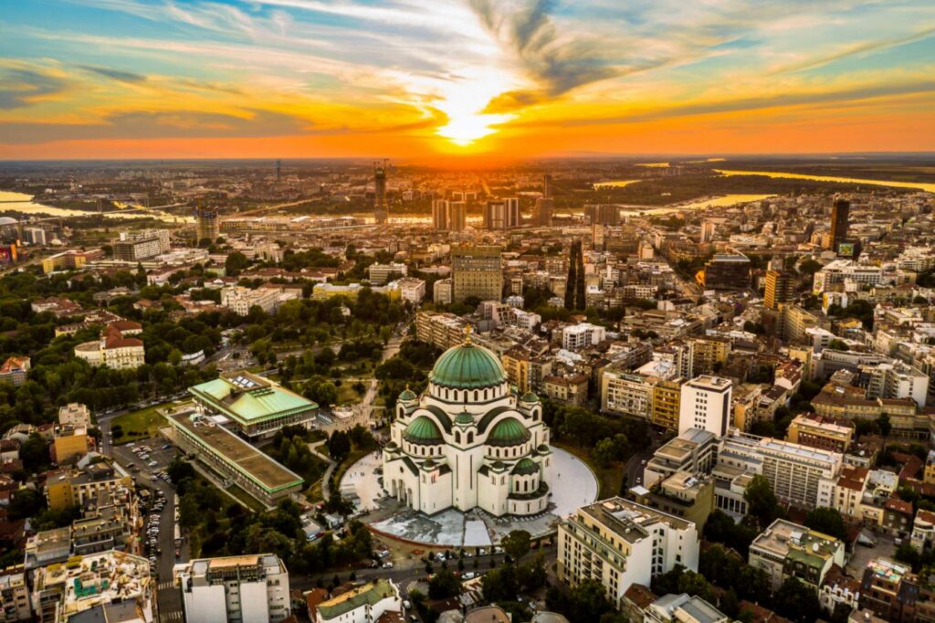 Luftaufnahme des St.-Sava-Tempels in Belgrad, Serbien, mit großer Kuppel, umgeben von Stadt und beleuchtet vom Sonnenuntergang.