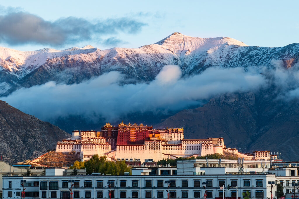 Potala-Palast in Lhasa, Tibet, China, mit weiß-roten Fassaden vor schneebedeckten Bergen und tief hängenden Wolken.