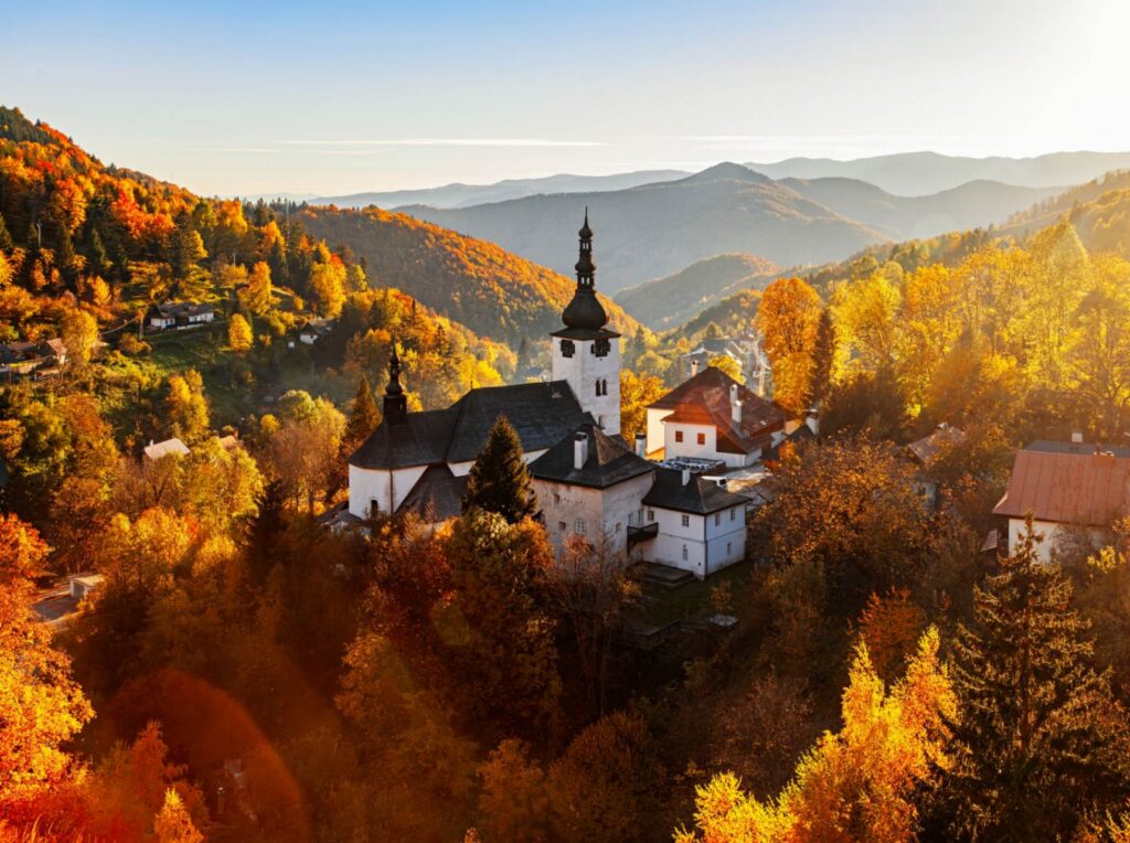 Kloster in Špania Dolina in der Slowakei, umgeben von bunten Herbstwäldern und sanften Bergen im warmen Sonnenlicht.