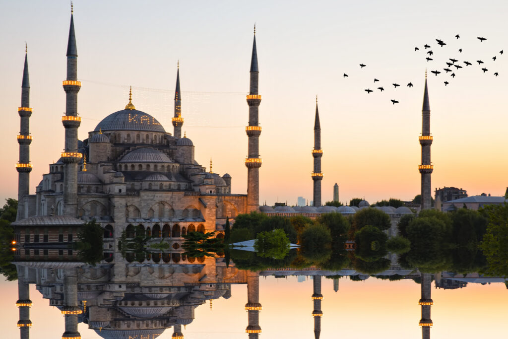 Blaue Moschee und Hagia Sophia in Istanbul, Türkei, bei Sonnenuntergang mit spiegelnder Wasserfläche und fliegenden Vögeln.