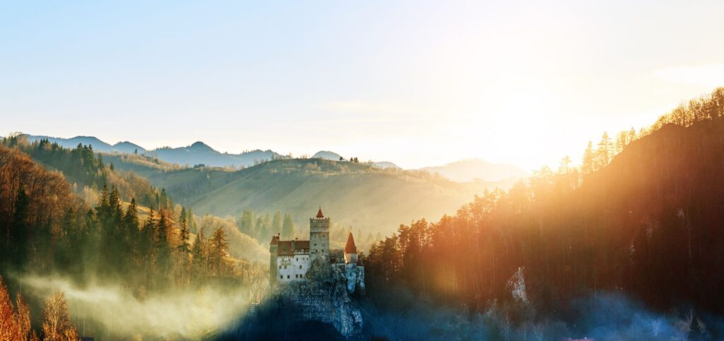 Schloss Bran in Rumänien auf einem Felsen, umgeben von Wald und Bergen bei Sonnenuntergang mit Nebel in den Tälern.