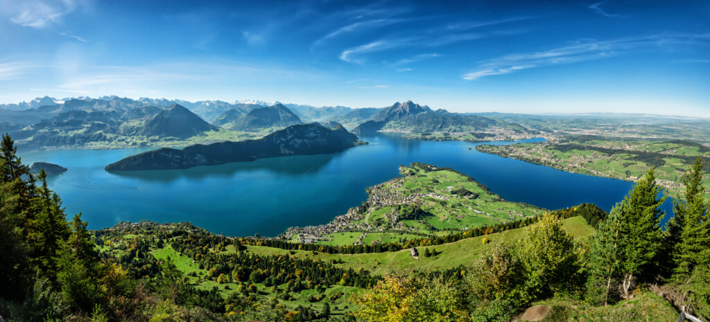 Panoramablick von der Rigi über den Vierwaldstättersee in der Schweiz mit dem Pilatus, grünen Hügeln, Dörfern und Alpen unter blauem Himmel.