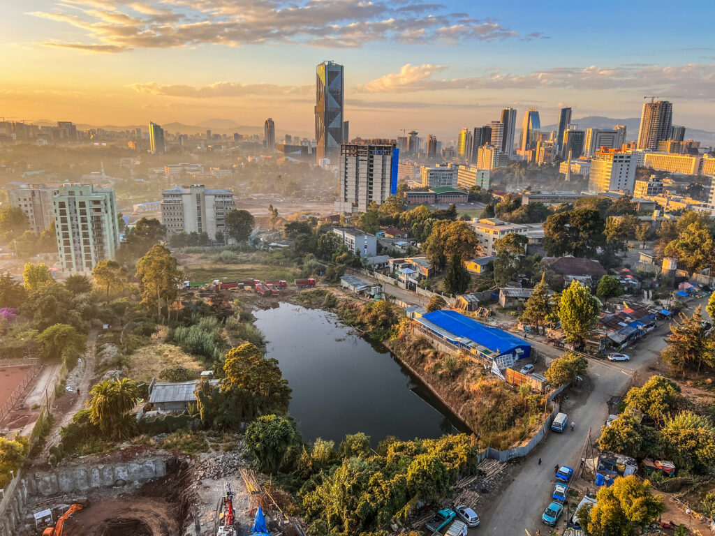 Luftaufnahme von Addis Abeba in Äthiopien mit modernen Hochhäusern, Neubauten, Wohnvierteln, Straßen und einem kleinen Gewässer im Vordergrund sowie der Skyline der Hauptstadt im Hintergrund.