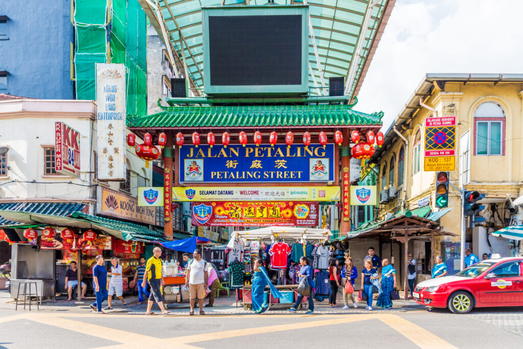 Eingangstor zur Petaling Street in Kuala Lumpurs Chinatown mit rotem Laternenschmuck, grünem Pagodendach und geschäftigem Straßenmarkt darunter.