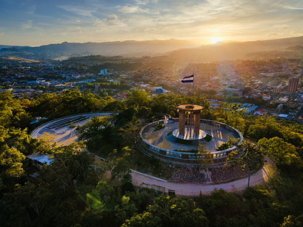 Luftaufnahme des modernisierten Aussichtspunkts auf dem Cerro Juana Laínez in Tegucigalpa, Honduras, mit kreisförmiger Aussichtsplattform, Nationalflagge und Blick über die Stadt bei Sonnenuntergang.