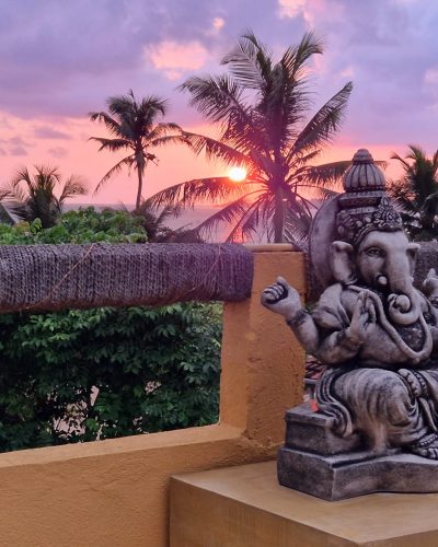 Ganesha-Statue auf einer Terrasse in Sri Lanka mit Palmen, Meer und farbenreichem Sonnenuntergang im Hintergrund.