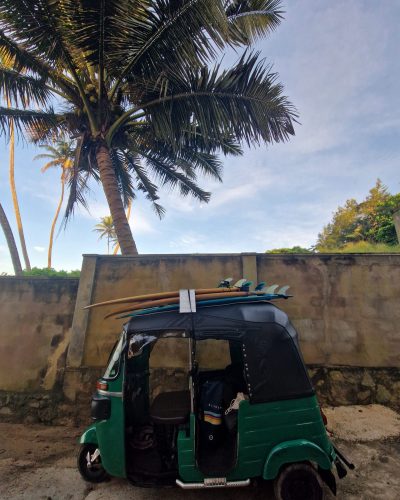 Grünes Tuk Tuk mit Surfboards auf dem Dach unter Kokospalmen an der Küste von Sri Lanka. Geben Sie Ihr Feedback zu BizChat ab.