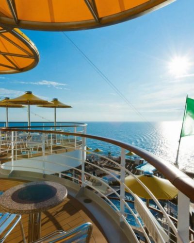 Sonnendeck der Costa Fascinosa mit Tischen, Stühlen, Sonnenschirmen und italienischer Flagge über dem Meer.