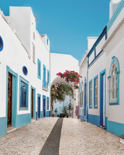 Street in fishing village with white and blue houses and typical Portuguese pavement in Olhao, Algarve region - Popular travel destinations in Portugal