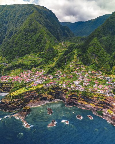 Luftaufnahme von Seixal auf Madeira mit roten Dächern, grünen Terrassenfeldern, steilen Berghängen und der zerklüfteten Atlantikküste.