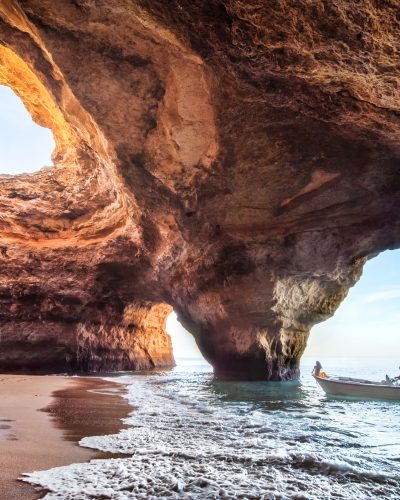 A boat navigates into the iconic Benagil Cave in Portugal, showcasing the cave's stunning rock formations and open ceiling. The sunlight streaming through the cave's skylight illuminates the natural beauty of this coastal marvel, making it a perfect destination for adventurers and nature lovers.