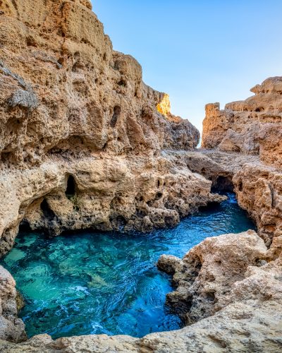 A stunning natural pool with crystal-clear turquoise water nestled among the rugged cliffs of Algar Seco in Carvoeiro, Algarve, Portugal. The rock formations surrounding the pool create a secluded and serene atmosphere, perfect for experiencing the raw beauty of the coast.