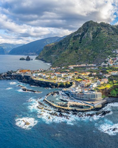Luftaufnahme von Porto Moniz auf Madeira mit natürlichen Lavapools, Küstendorf, Atlantik, schroffen Vulkanfelsen und grünen Berghängen im Hintergrund.