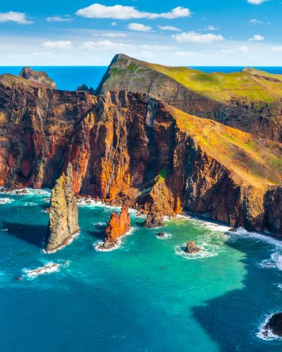 Luftaufnahme des Kaps Ponta de São Lourenço auf Madeira mit steilen Felsklippen, vorgelagerten Felsnadeln und türkisblauem Atlantik unter einem sonnigen Himmel.