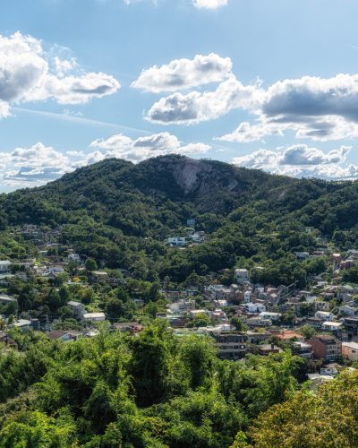 Blick auf den Inwangsan-Berg in Seoul mit bewaldeten Hängen, markanter Granitfelswand, Wohnhäusern im Stadtteil Buam-dong und einem blauen Himmel mit großen weißen Wolken.