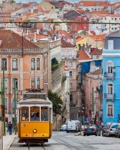 Classic traditional yellow trolley tram 28 in Lisbon on a hill with cityscape and colorful houses in the distance, Portugal 25 May 2012