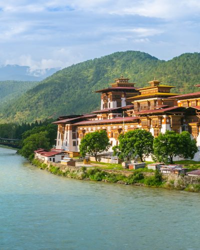 Punakha Dzong in Bhutan am Zusammenfluss von Pho Chhu und Mo Chhu, umgeben von grünen Bergen, Bäumen und einer idyllischen Flusslandschaft.