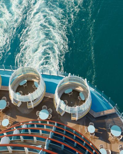Außendeck der Costa Smeralda mit runden Lounge-Bereichen, Tischen und Blick auf das türkisblaue Meer sowie das Kielwasser.
