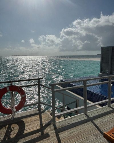 Terrasse einer Wasservilla auf den Malediven mit Treppe zum Meer, Poolbereich und Blick auf den glitzernden Indischen Ozean.