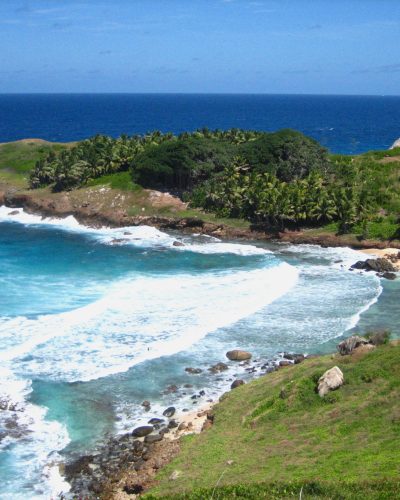 Kleine tropische Bucht mit Sandstrand, türkisfarbenem Wasser und palmenbewachsener Küste.